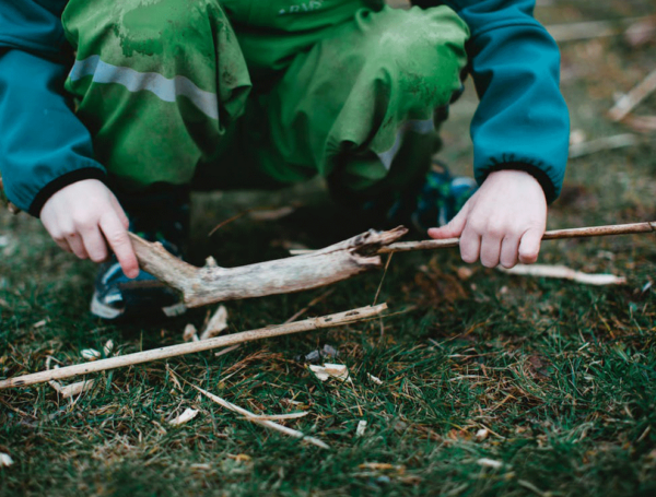 Foto van een hurkend kind in het bos met houten takjes