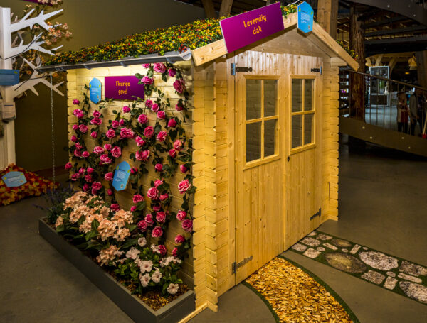 Houten tuinhuisje van de expositie 'Ga voor groen' in het Duurzaamheidscentrum Assen. Aan de zijkant zie je een zelf-doe-tip, namelijk het maken van een bloemrijke geveltuin.