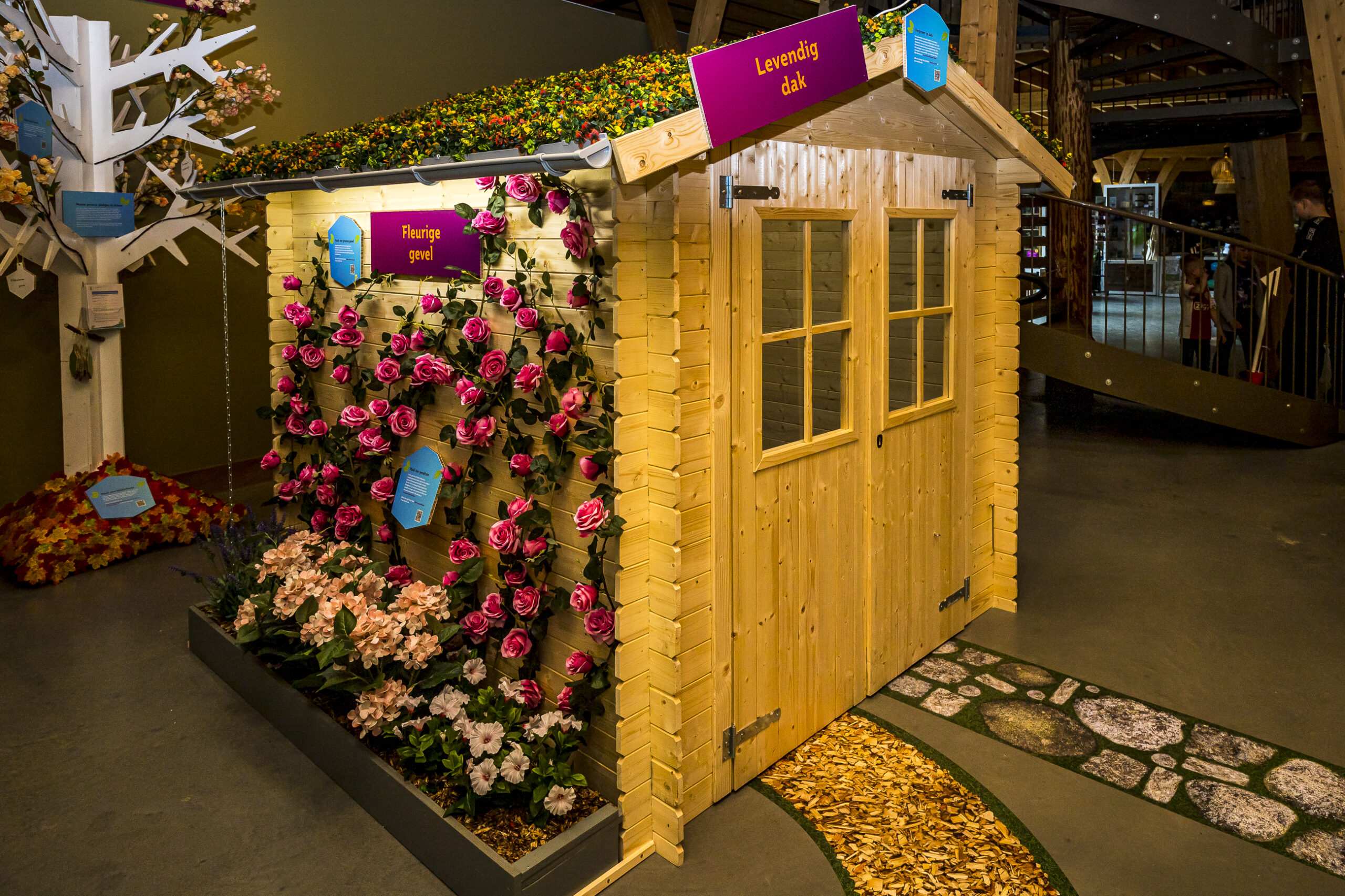 Houten tuinhuisje van de expositie 'Ga voor groen' in het Duurzaamheidscentrum Assen. Aan de zijkant zie je een zelf-doe-tip, namelijk het maken van een bloemrijke geveltuin.