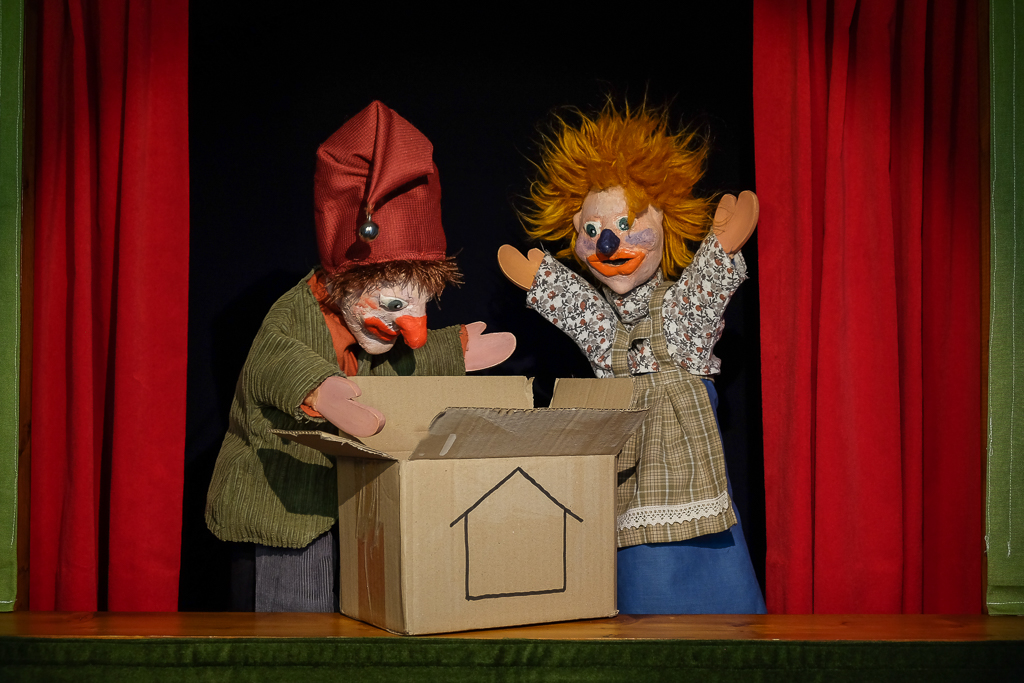 Poppen Jan Klaassen en Katrijn met een verhuisdoos op het podium. De link gaat naar de activiteit Jan Klaassen en de verhuismuis.