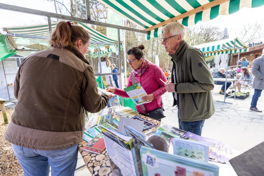 Twee bezoekers kijken naar wat een medewerker van Landschapsbeheer Drenthe laat zien.