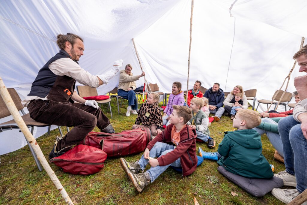 Kinderen kijken naar de voorstelling 'tot op de bodem' onder een groot wit doek.