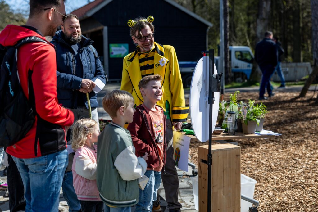 Een kind draait aan het rad van fortuin. Man met een bijenpak aan staat er bij te kijken.