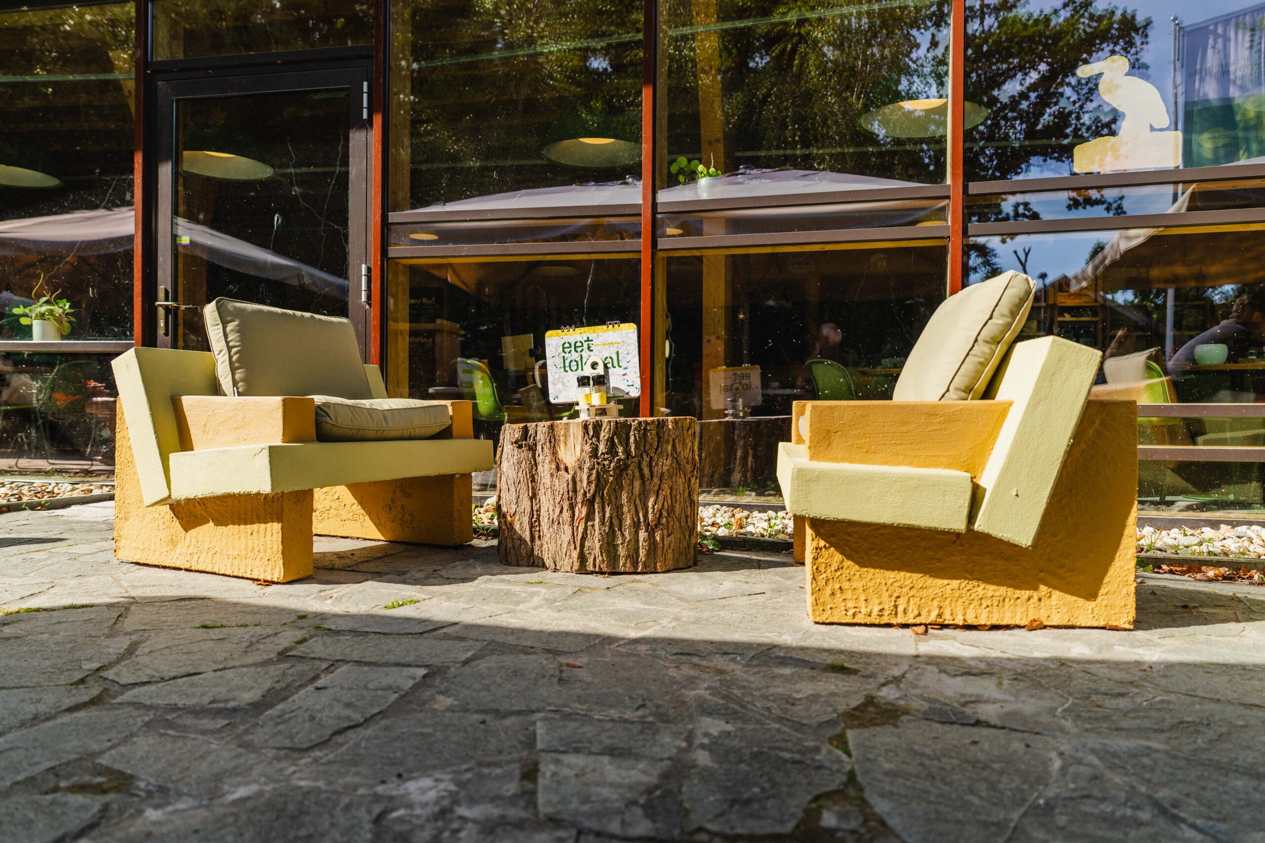 Terras van het Duurzaamheidscentrum Assen. Twee loungestoelen met een boomstamtafeltje met menukaart